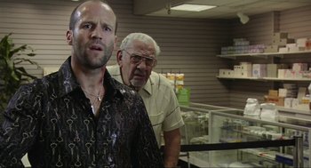 Movie still from “Crank” (2006), directed by Mark Neveldine – A man standing next to another man in front of a display case; Close Up shot, Over the shoulder angle