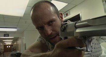 Movie still from “Crank” (2006), directed by Mark Neveldine – A man holding a gun in a room; Close Up shot, Low angle