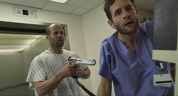 Movie still from “Crank” (2006), directed by Mark Neveldine – A man in a hospital gown holding a gun next to another man in a hospital gown; Medium shot, Low angle
