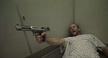 Movie still from “Crank” (2006), directed by Mark Neveldine – A man is holding a gun up to his face; Medium shot, Overhead angle