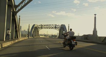 Movie still from “Crank” (2006), directed by Mark Neveldine – A man riding a motorcycle across a bridge; Extreme Wide shot, Low angle