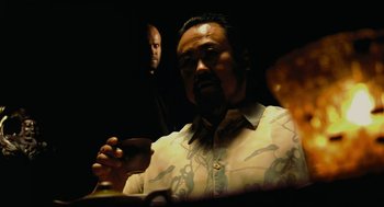 Movie still from “Crank” (2006), directed by Mark Neveldine – A man sitting at a table holding a wine glass; Medium shot, Over the shoulder angle