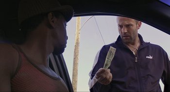 Movie still from “Crank” (2006), directed by Mark Neveldine – A man holding a dollar bill in front of another man in the back of a car; Close Up shot, Over the shoulder angle