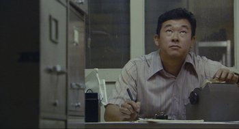 Movie still from “Crank” (2006), directed by Mark Neveldine – A man sitting at a table writing on a piece of paper; Close Up shot, Low angle