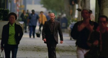 Movie still from “Crank” (2006), directed by Mark Neveldine – A man walking down the street wearing a suit and tie; Wide shot, Low angle