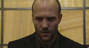 Movie still from “Crank” (2006), directed by Mark Neveldine – A man in a suit and tie looking at the camera; Close Up shot, Low angle