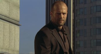 Movie still from “Crank” (2006), directed by Mark Neveldine – A man in a suit and tie standing in front of a tall building; Close Up shot, Low angle