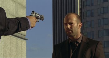 Movie still from “Crank” (2006), directed by Mark Neveldine – A man holding a gun pointed at a man in a suit and tie; Medium shot, Over the shoulder angle