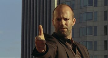 Movie still from “Crank” (2006), directed by Mark Neveldine – A man giving a thumbs up in front of a tall building; Close Up shot, Low angle