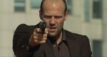 Movie still from “Crank” (2006), directed by Mark Neveldine – A man in a suit and tie holding a gun; Close Up shot, Low angle