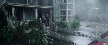 Movie still from “Crawl” (2019), directed by Alexandre Aja – Two people sitting on the steps of a house in the pouring rain; Extreme Wide shot, High angle