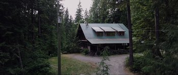 Movie still from “Crawlspace” (2022), directed by L. Gustavo Cooper – A house in the middle of a forest with a power line; Extreme Wide shot, High angle