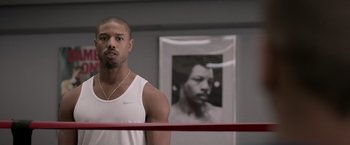 Movie still from “Creed” (2015), directed by Ryan Coogler – A man standing in a boxing ring in front of a picture of himself; Close Up shot, Over the shoulder angle