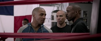 Movie still from “Creed” (2015), directed by Ryan Coogler – A group of men standing next to each other in front of a punching bag; Close Up shot, Over the shoulder angle