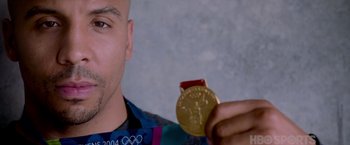 Movie still from “Creed” (2015), directed by Ryan Coogler – A man holding up a gold medal in front of his face; Close Up shot, Low angle
