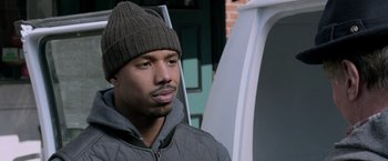Movie still from “Creed” (2015), directed by Ryan Coogler – A person wearing a jacket and a hat; Close Up shot, Over the shoulder angle