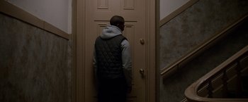 Movie still from “Creed” (2015), directed by Ryan Coogler – A man standing in front of a door in a room; Medium shot, Over the shoulder angle