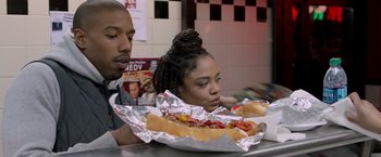 Movie still from “Creed” (2015), directed by Ryan Coogler – A man and a woman sitting in front of a hot dog; Medium shot, Over the shoulder angle