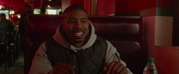 Movie still from “Creed” (2015), directed by Ryan Coogler – A man sitting in a booth smiling for the camera; Close Up shot, Over the shoulder angle