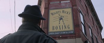 Movie still from “Creed” (2015), directed by Ryan Coogler – A man wearing a black hat standing in front of a boxing gym sign; Wide shot, High angle