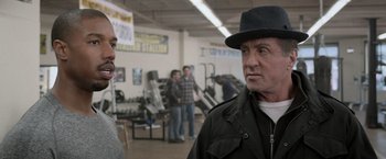 Movie still from “Creed” (2015), directed by Ryan Coogler – A man wearing a black hat talking to another man in a gym; Close Up shot, Over the shoulder angle
