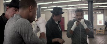 Movie still from “Creed” (2015), directed by Ryan Coogler – A group of men standing around each other in a room; Medium shot, Over the shoulder angle