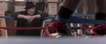 Movie still from “Creed” (2015), directed by Ryan Coogler – A man in a boxing ring holding a rope; Medium shot, Over the shoulder angle