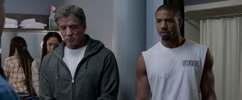 Movie still from “Creed” (2015), directed by Ryan Coogler – Two men standing next to each other in front of a wall; Medium shot, Over the shoulder angle