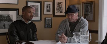 Movie still from “Creed” (2015), directed by Ryan Coogler – Two men sitting at a table in front of pictures; Medium shot, Over the shoulder angle
