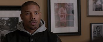 Movie still from “Creed” (2015), directed by Ryan Coogler – A man standing in front of a picture of a man in a robe; Close Up shot, Over the shoulder angle
