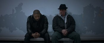 Movie still from “Creed” (2015), directed by Ryan Coogler – Two men sitting next to each other on a bench; Medium shot, Over the shoulder angle