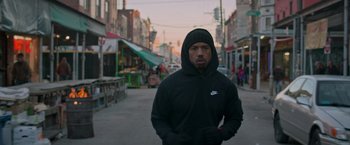Movie still from “Creed” (2015), directed by Ryan Coogler – A man wearing a black hoodie standing in the middle of a street; Medium shot, Over the shoulder angle