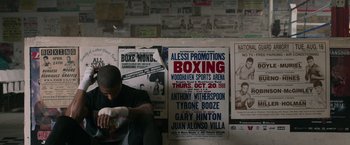 Movie still from “Creed” (2015), directed by Ryan Coogler – A man in a boxing ring next to a wall of posters; Wide shot, High angle