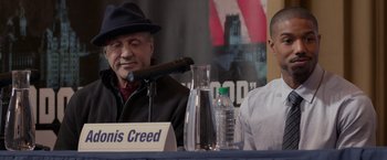 Movie still from “Creed” (2015), directed by Ryan Coogler – Two men sitting at a table in front of microphones; Close Up shot, Over the shoulder angle