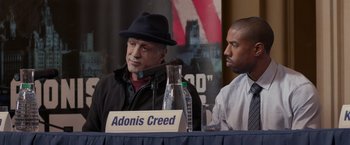 Movie still from “Creed” (2015), directed by Ryan Coogler – Two men sitting at a table with a microphone; Close Up shot, Over the shoulder angle
