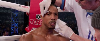Movie still from “Creed” (2015), directed by Ryan Coogler – A man getting his face waxed in a boxing ring; Close Up shot, Over the shoulder angle