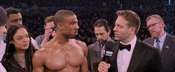 Movie still from “Creed” (2015), directed by Ryan Coogler – A man is being interviewed in a boxing ring; Medium shot, Over the shoulder angle