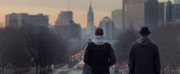 Movie still from “Creed” (2015), directed by Ryan Coogler – A man standing on the side of a road looking at a city skyline; Wide shot, Over the shoulder angle