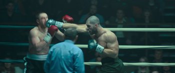 Movie still from “Creed II” (2018), directed by Steven Caple Jr. – A man in a boxing ring hitting another man with a punch; Medium shot, Over the shoulder angle