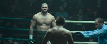 Movie still from “Creed II” (2018), directed by Steven Caple Jr. – A man standing in a boxing ring looking at another man in a boxing ring; Medium shot, Over the shoulder angle