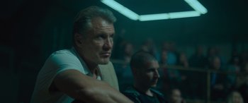 Movie still from “Creed II” (2018), directed by Steven Caple Jr. – A man sitting in front of a crowd of people in a room; Close Up shot, Low angle