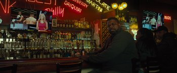 Movie still from “Creed II” (2018), directed by Steven Caple Jr. – A man sitting in front of a bar with bottles of alcohol behind him; Medium shot, Low angle
