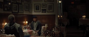 Movie still from “Creed II” (2018), directed by Steven Caple Jr. – A man sitting at a table in front of a bunch of tables; Wide shot, Over the shoulder angle