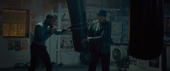 Movie still from “Creed II” (2018), directed by Steven Caple Jr. – A man in a hat and a jacket is hitting a punching bag; Wide shot, High angle