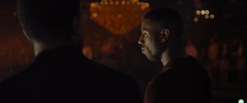 Movie still from “Creed II” (2018), directed by Steven Caple Jr. – A man in a red shirt is in a dark room; Close Up shot, Over the shoulder angle