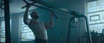 Movie still from “Creed II” (2018), directed by Steven Caple Jr. – A man doing pull - ups on a bar in a gym; Medium shot, Low angle