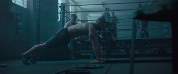 Movie still from “Creed II” (2018), directed by Steven Caple Jr. – A man in a boxing ring doing push - ups; Wide shot, Over the shoulder angle