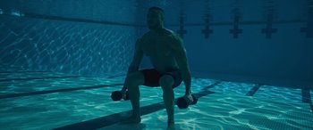 Movie still from “Creed II” (2018), directed by Steven Caple Jr. – A man in the water holding two dumbbells; Wide shot, High angle