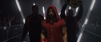Movie still from “Creed II” (2018), directed by Steven Caple Jr. – A man in a red hooded sweatshirt stands in front of a crowd; Medium shot, Low angle