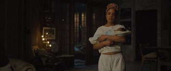 Movie still from “Creed II” (2018), directed by Steven Caple Jr. – A woman holding a baby in her arms in a living room; Medium shot, Over the shoulder angle